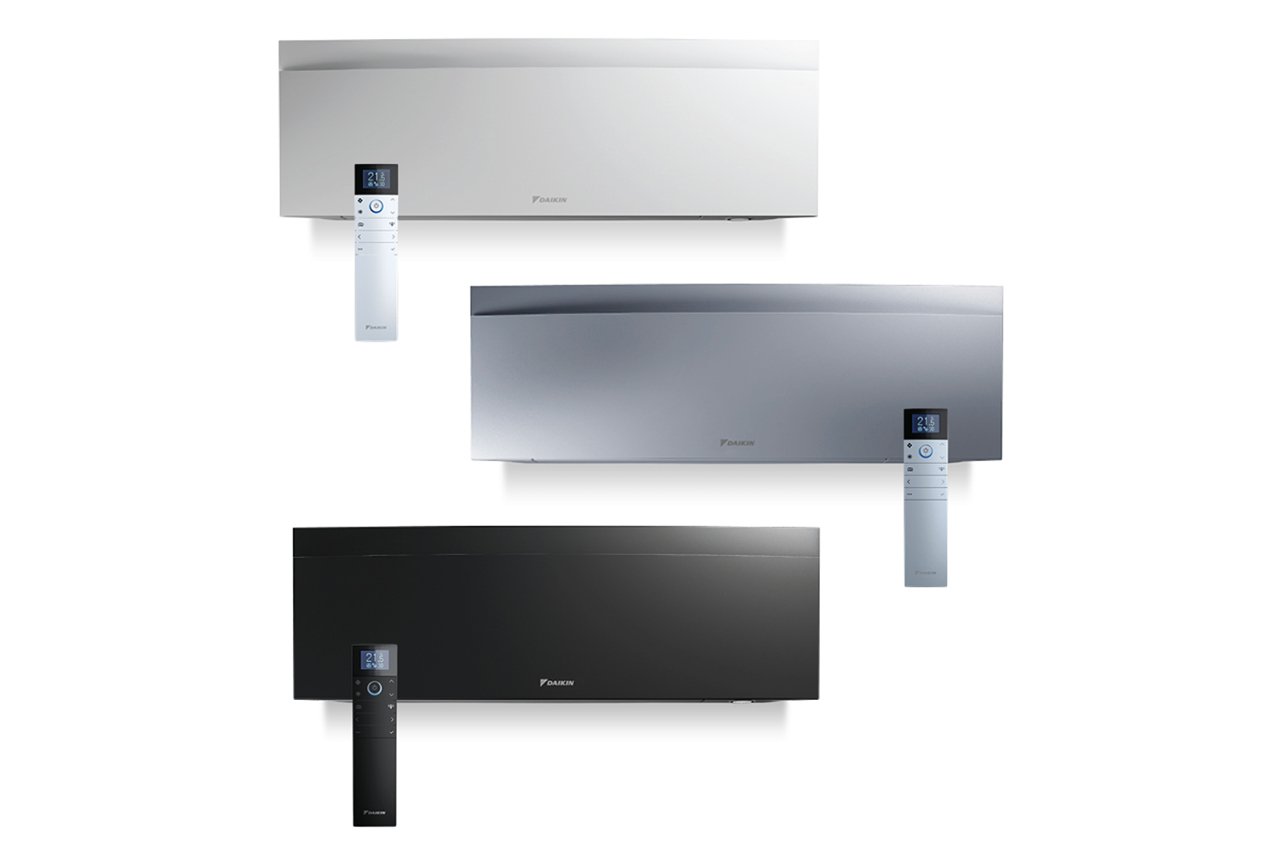 Tre njësi të kondicionerit Daikin Emura 3 të montuara në mur, në ngjyrë të bardhë, argjendtë dhe të zezë, secila me telekomandë dixhitale përpara.